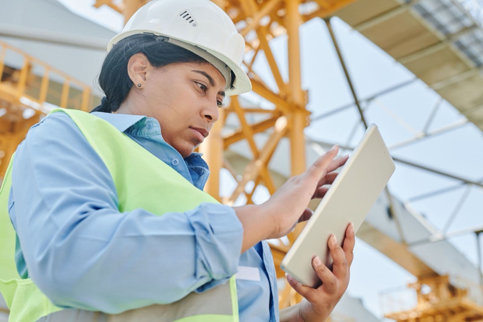 Engenheira de capacete usando software de gestão em tablet no canteiro de obras